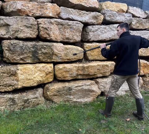 James Dorkel, de dos, nettoie à la lance un mur de gros blocs de pierre calcaire